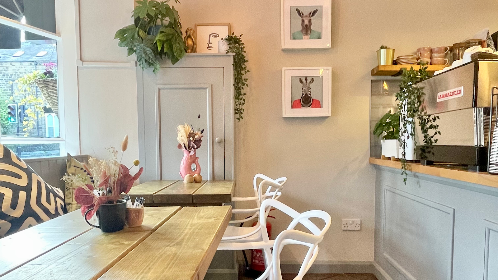 The interior of Arlo café with wooden tables, animal-portrait wall art, trailing plants, and espresso bar.
