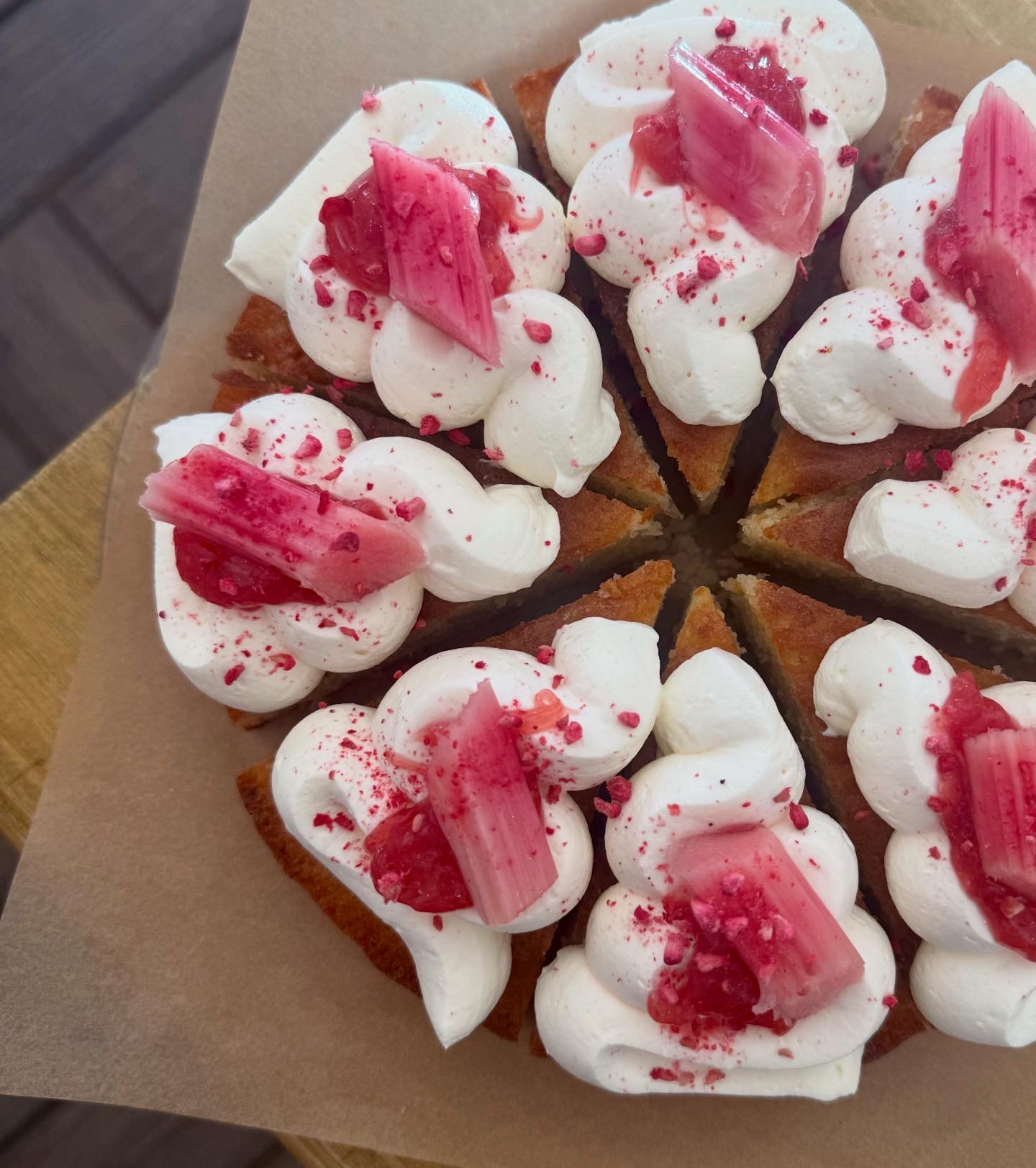 A whole pre-sliced cake topped with cream rosettes, poached rhubarb, and freeze-dried berry dust.