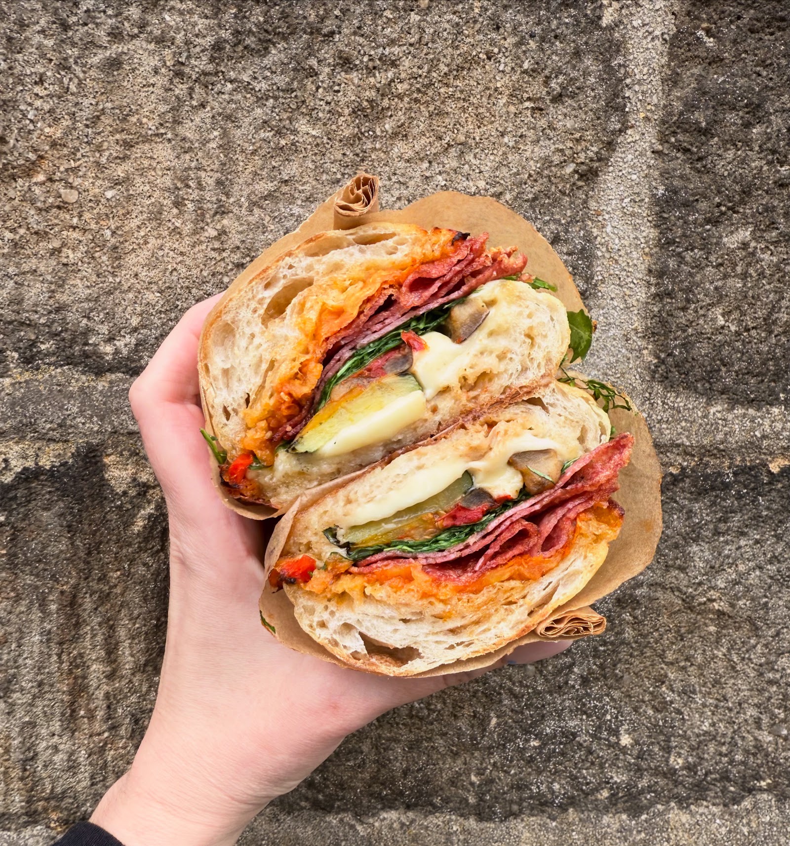 A halved loaded ciabatta sandwich with salami, egg, greens, and melted cheese.